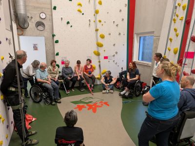 Teilnehmende der MS-Klettergruppe „Move & Climb MS“ sitzen im Kreis in der Kletterhalle Dachau und bereiten sich gemeinsam auf das Klettern vor.